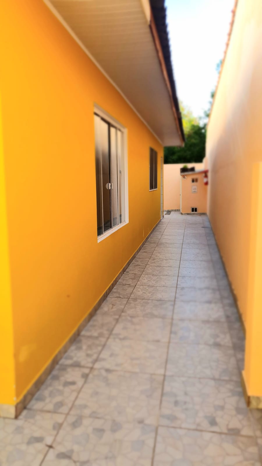 Corredor lateral externo com piso cerâmico e paredes amarelas