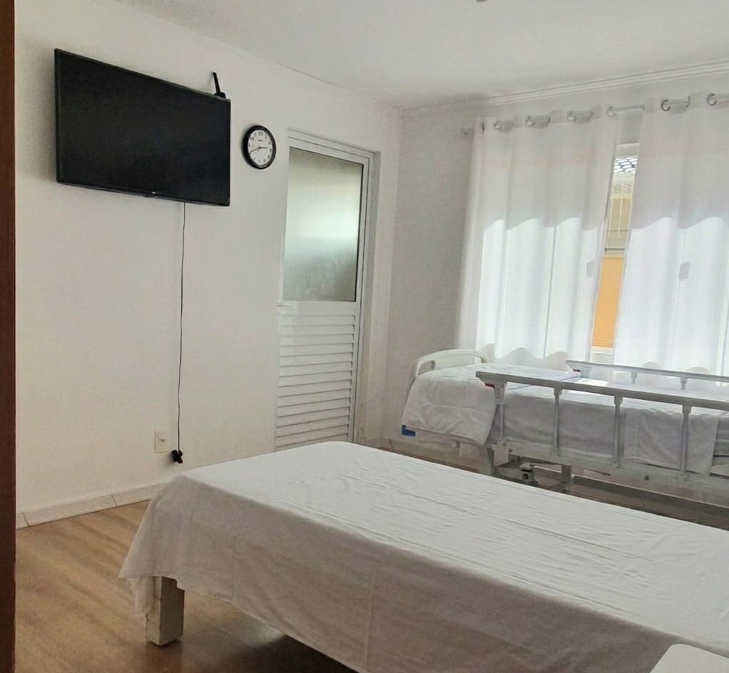Quarto com cama hospitalar articulada e TV para conforto do morador