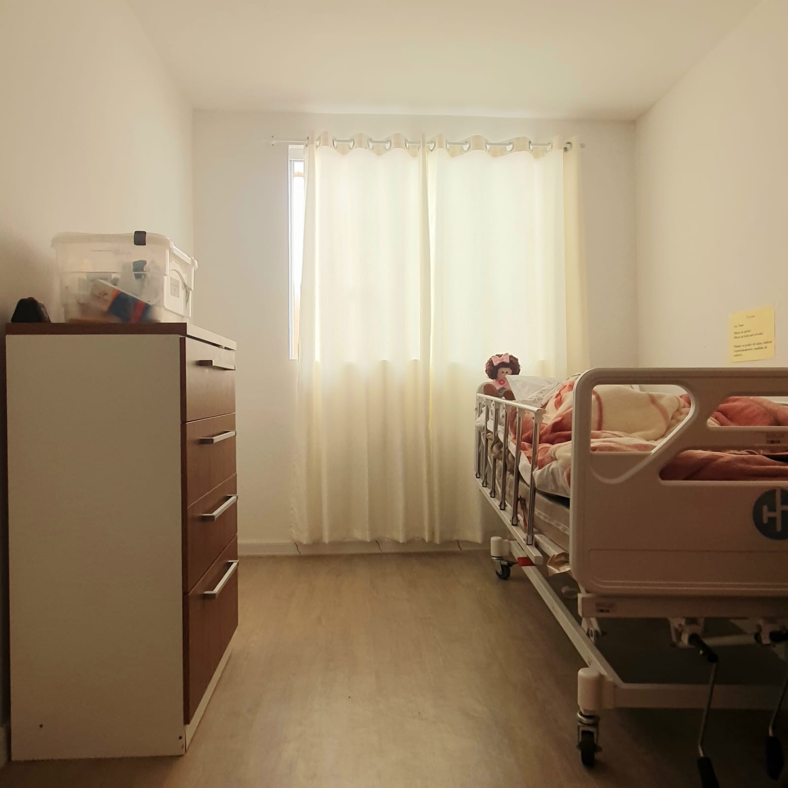 Quarto com cama hospitalar, cômoda e boa iluminação natural